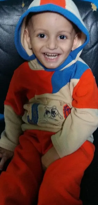 Happy child in colorful hoodie smiling in front of a blue wall.