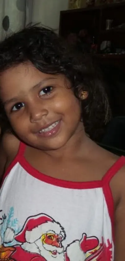 Young child with curly hair in a festive red outfit smiling warmly at home.