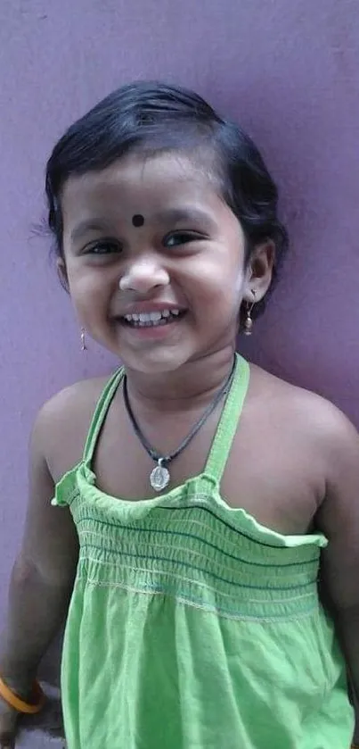 Smiling child in green dress with lavender background.