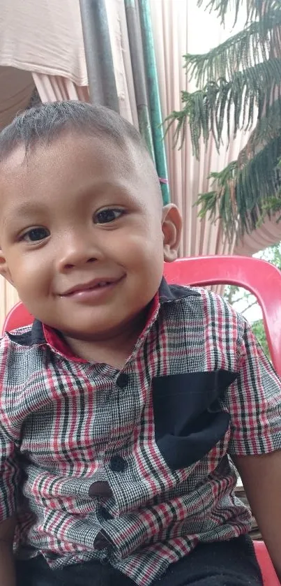 Smiling child in plaid shirt on red chair outdoors.