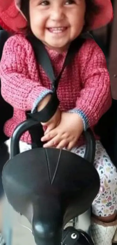 Smiling child in a red hat and sweater sitting joyfully.