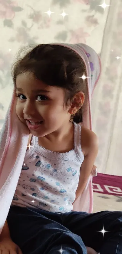 Smiling child with light pink blanket indoors.