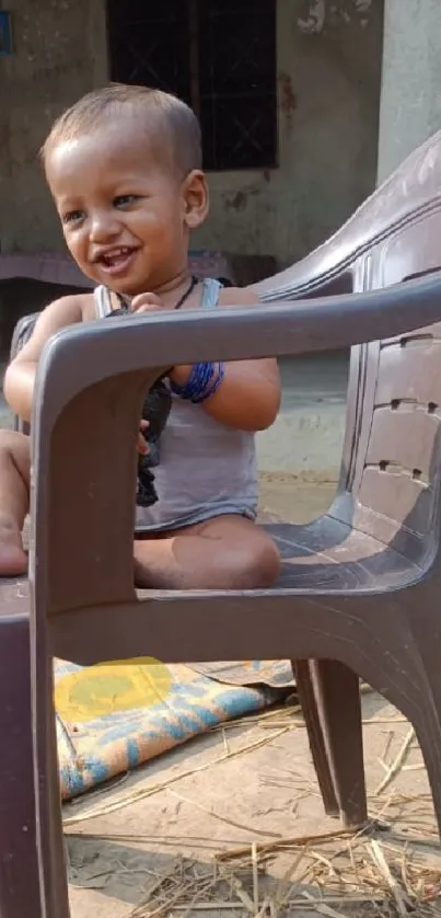 Smiling child sitting on a brown plastic chair outside.