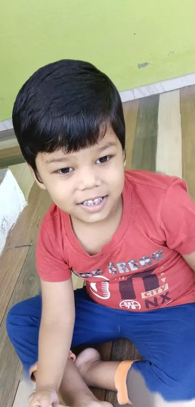 Smiling child in red shirt sitting on a colorful wooden floor.