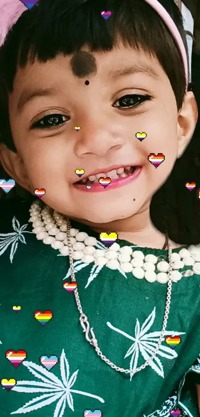 Smiling child in green outfit with hearts.