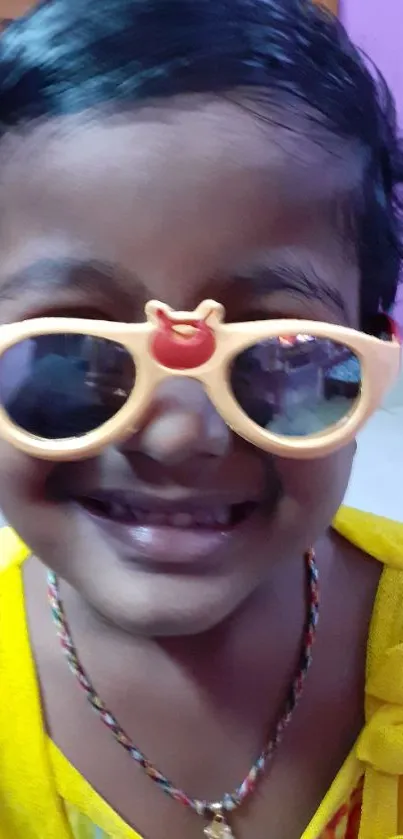 Smiling child in yellow shirt with sunglasses.