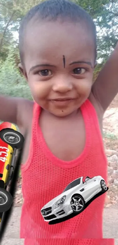 Smiling child in red vest with toy cars on a sunny day.