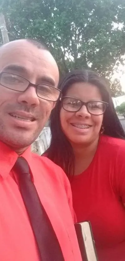 Couple smiling in an outdoor setting, dressed in red attire.