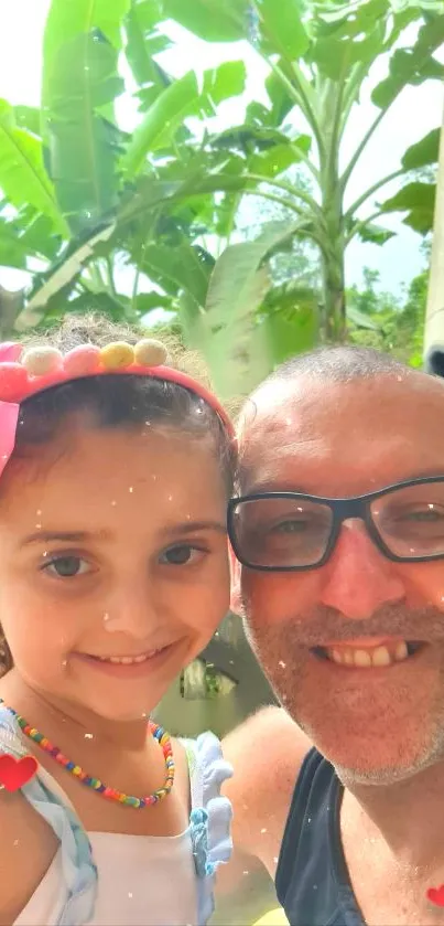 Father and daughter smiling outdoors with green foliage backdrop.