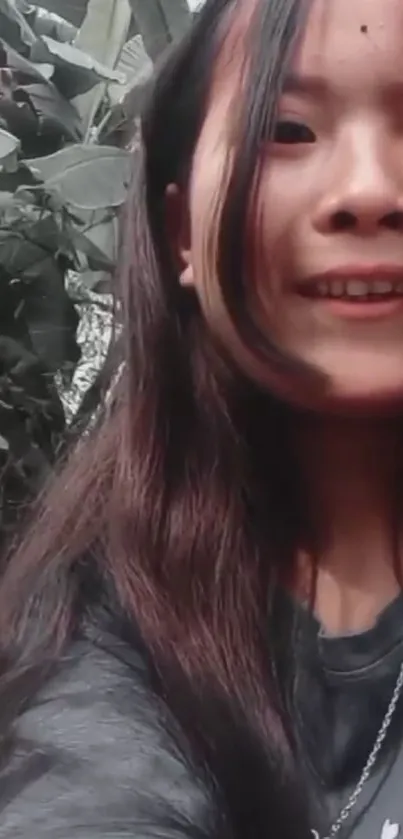 Smiling girl with long hair among green leaves.