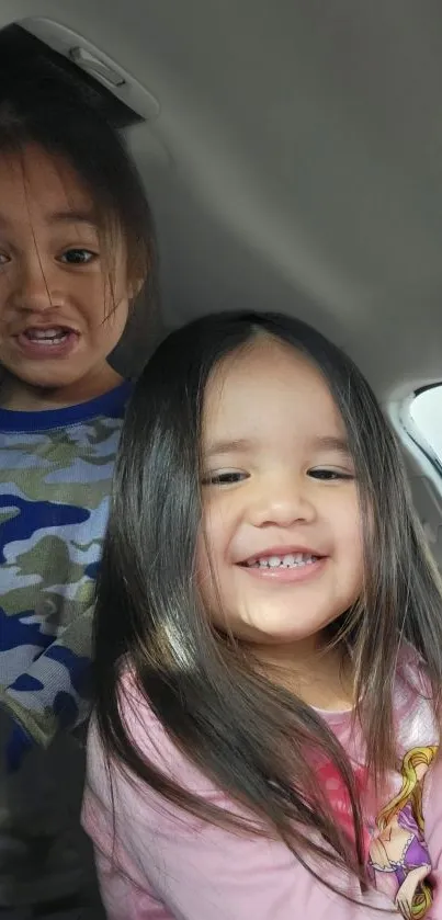 Two smiling children posing inside a car.