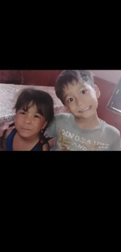 Two smiling children sitting together on a cozy bed.