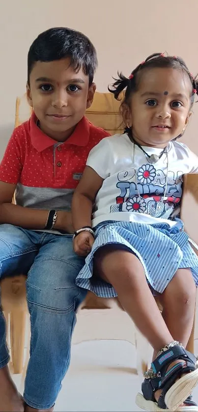 Two children smiling on a wooden chair.