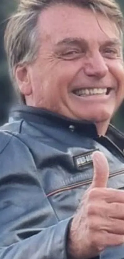 Man smiling in leather jacket with thumbs up in outdoor setting.