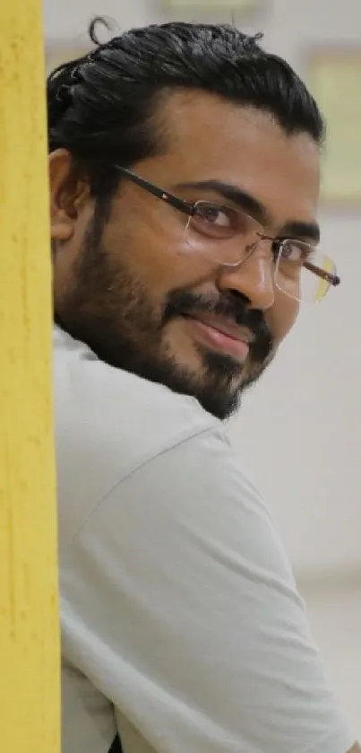 Portrait of a smiling man with glasses against a yellow background.