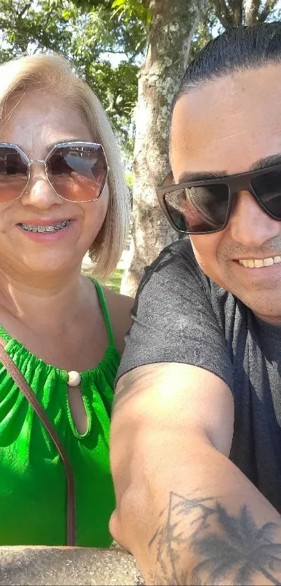 Two people smiling in a sunny park with trees.