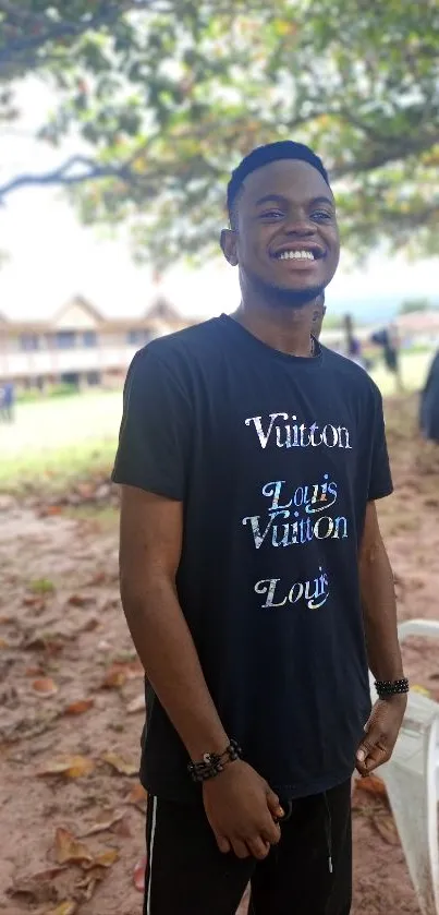 A person smiling under trees in a natural outdoor setting.