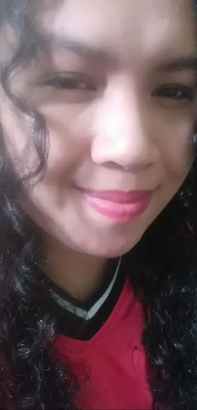 Close-up portrait of a smiling person with curly hair and pink shirt.