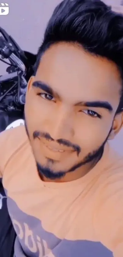 Man smiling in selfie with motorbike, light brown tones.