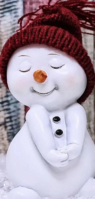 Smiling snowman figurine with red hat on a wooden background.