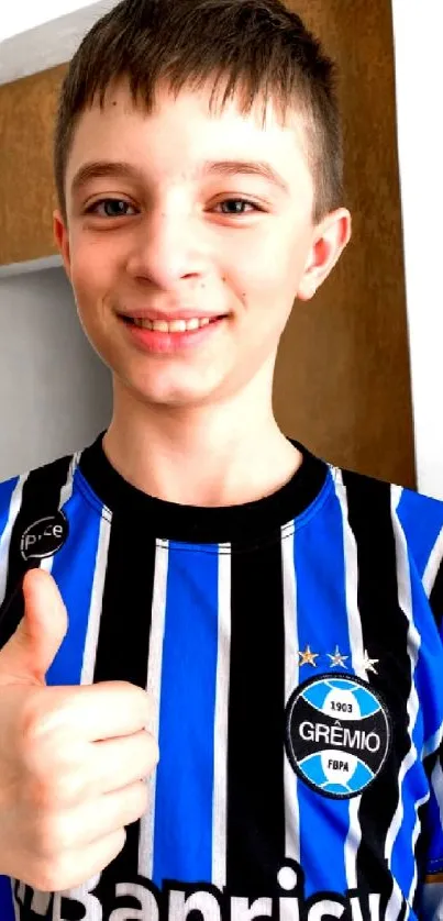 Young soccer fan giving thumbs up in blue striped jersey.