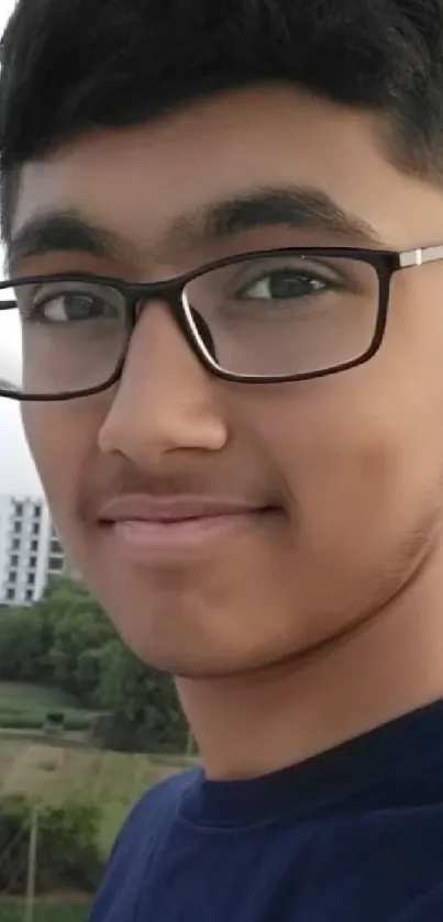 Portrait of a smiling teenage boy with glasses against a city background.