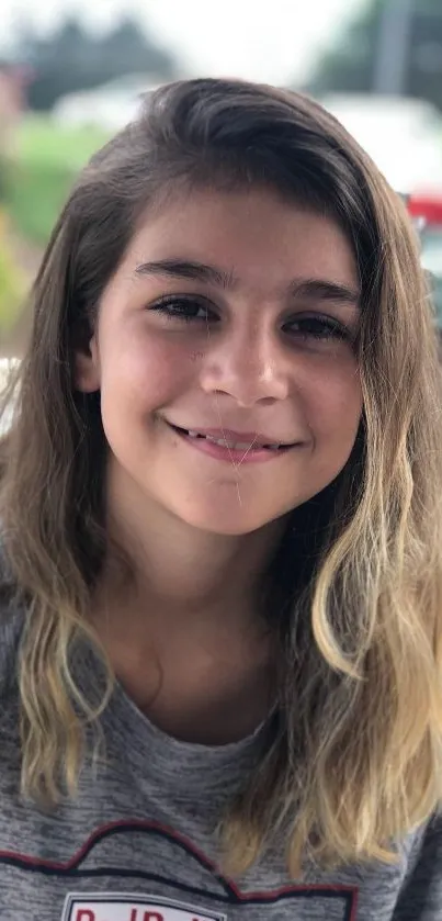 Smiling teen with flowing hair in a casual outdoor setting.