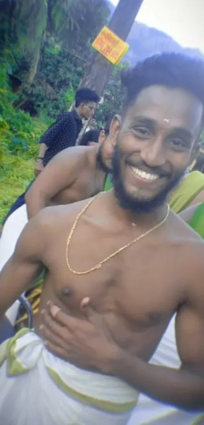 Man in traditional attire smiling outdoors with greenery.