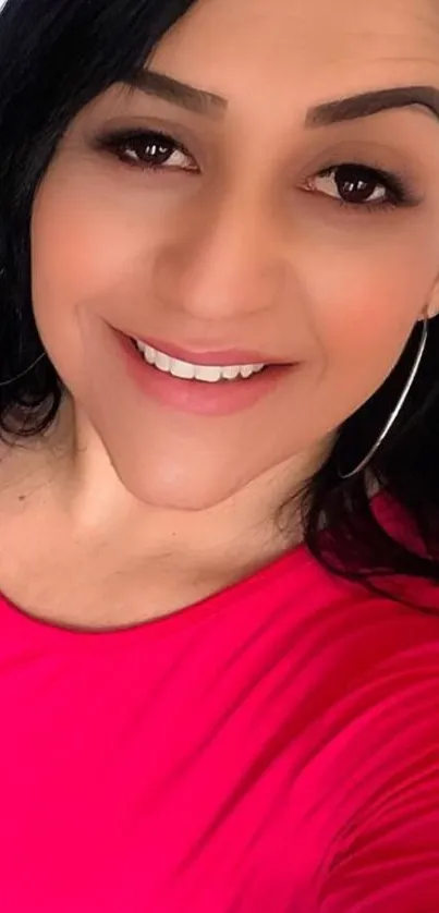 Woman smiling in bright pink shirt with natural makeup and hoop earrings.