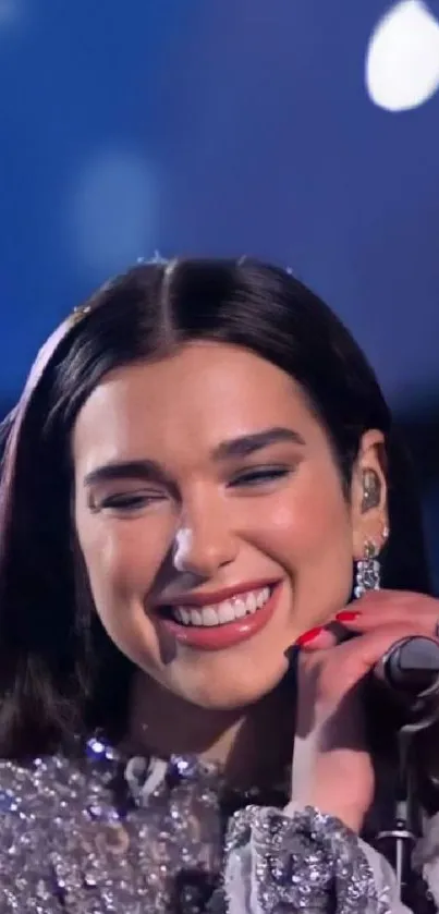 Woman singing on stage, wearing a sparkling dress, with a vibrant smile.