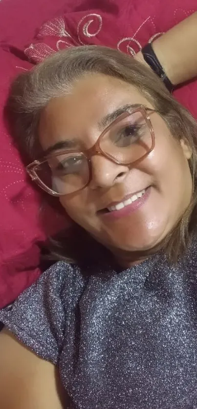 Woman smiling with glasses, lying on a red pillow.