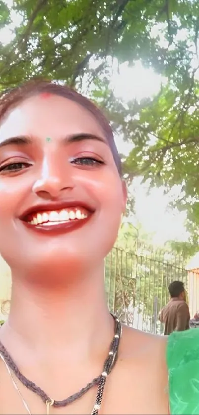 Woman smiling under green tree canopy.