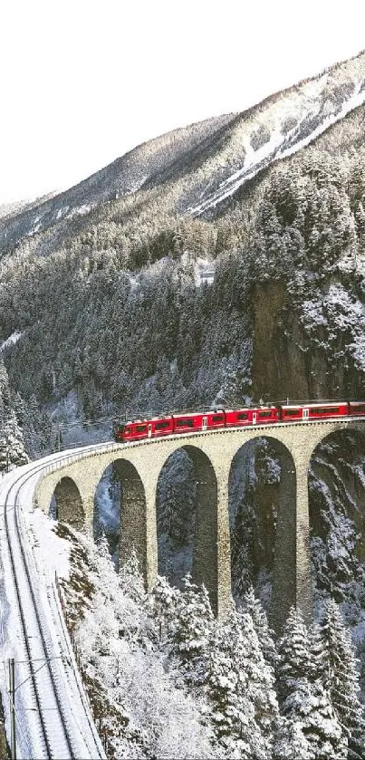 Red train on a snowy mountain viaduct, serene winter landscape.