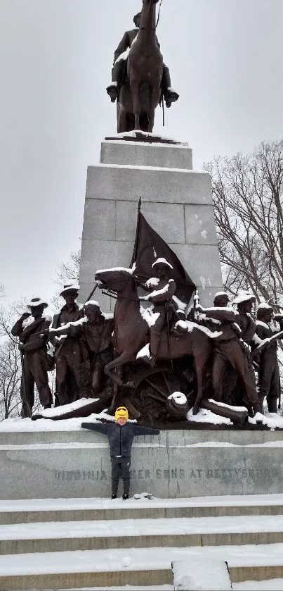 Snow-covered bronze monument with winter trees.