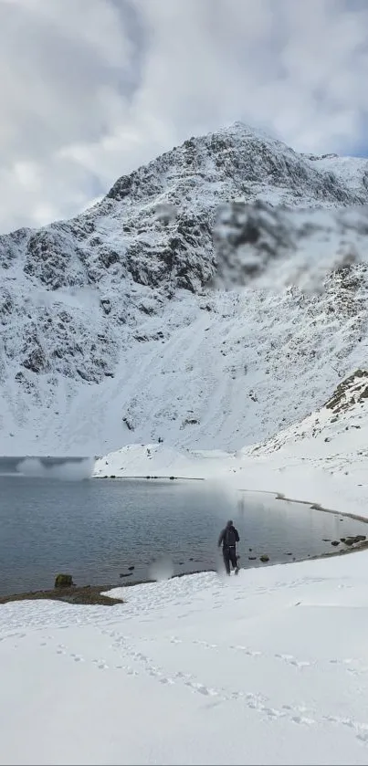 A lone figure walks through a snowy mountain landscape beside a calm lake.