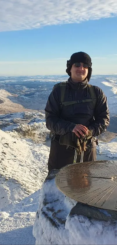 Person stands atop snow-covered mountain with clear blue sky.