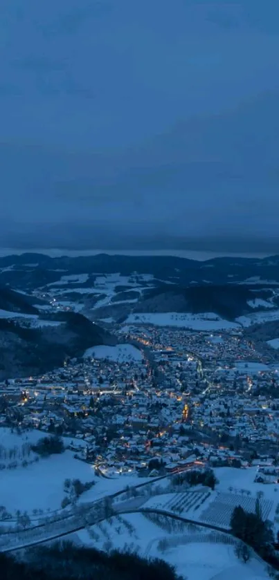 Aerial view of a snowy city at night with blue tones and glowing lights.