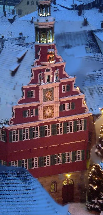 Snowy townscape with a red building and illuminated Christmas tree at night.