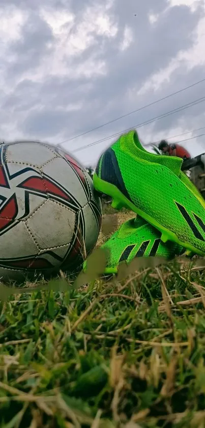Soccer ball and neon green cleats on grass under a cloudy sky.