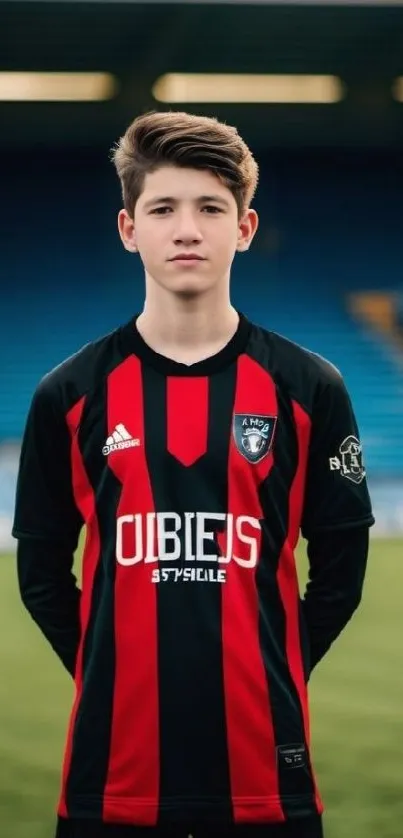 Young soccer player standing on field in a red and black uniform.