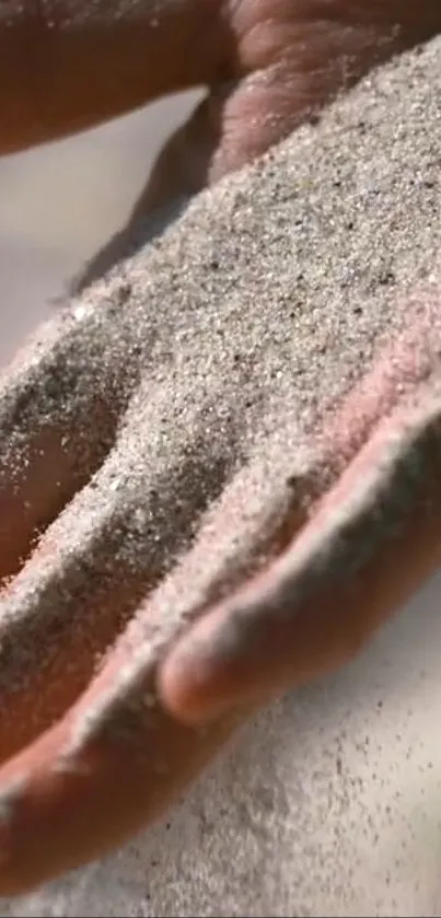 A hand gently letting fine sand slip through fingers in soft sunlight.