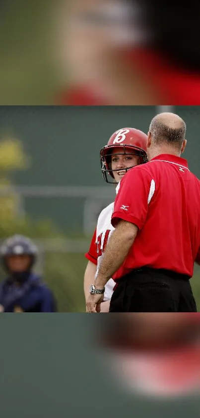 Softball player and coach in red talking on field with helmet.