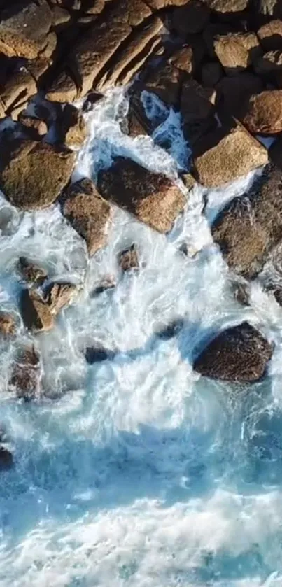 Aerial view of ocean waves crashing over rugged coastal rocks in blue hues.