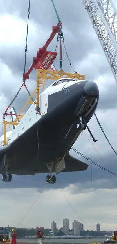 Space shuttle being lifted by crane in urban setting.