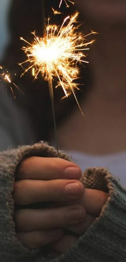 A close-up of hands holding a glowing sparkler in a cozy, dark setting.