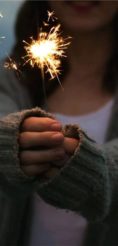 A cozy hand holds a brightly lit sparkler in a soft, textured sweater against a dark backdrop.