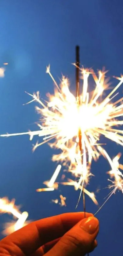 Hand holding a bright sparkler against a blue sky backdrop.