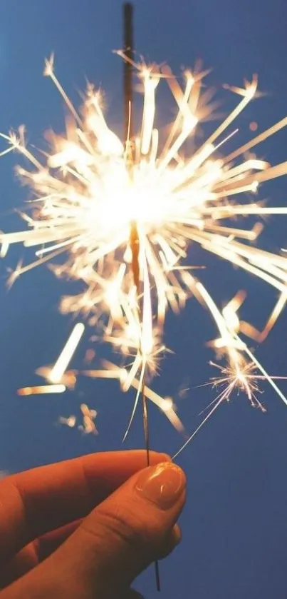 A hand holding a lit sparkler on a blue background.