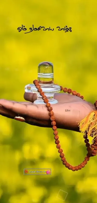 Hand holding lingam with beads on yellow background.