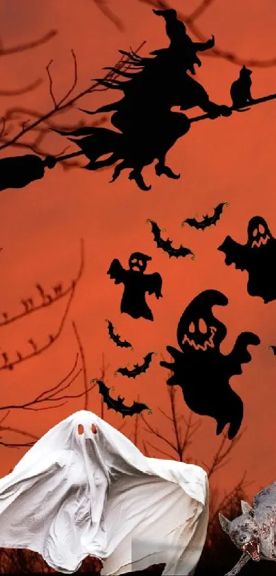 Halloween scene with witch, ghosts, and bats against orange sky.